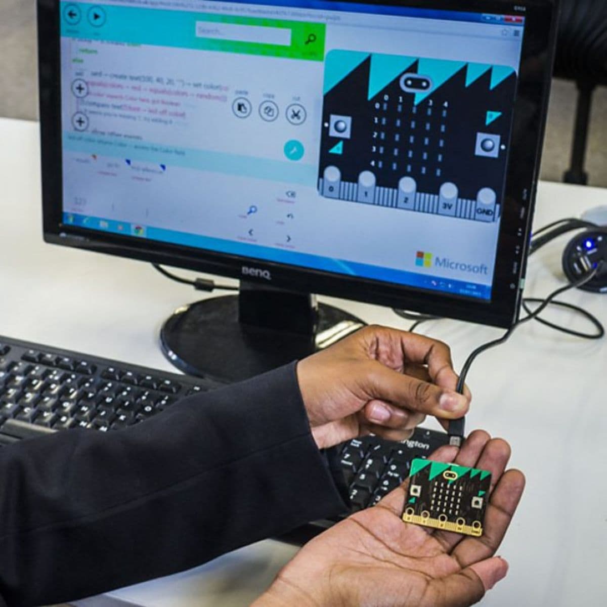 Girl holding a micro:bit board in front of a computer screen