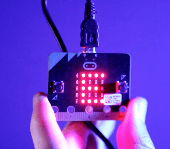 micro:bit board with glowing red LEDs displaying a message