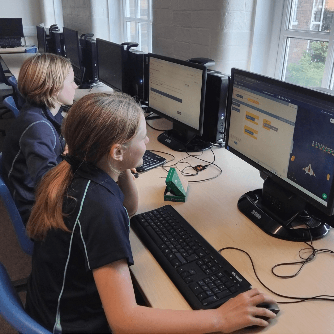 Two girls at desktop computers coding with MakeCode in a school computer lab