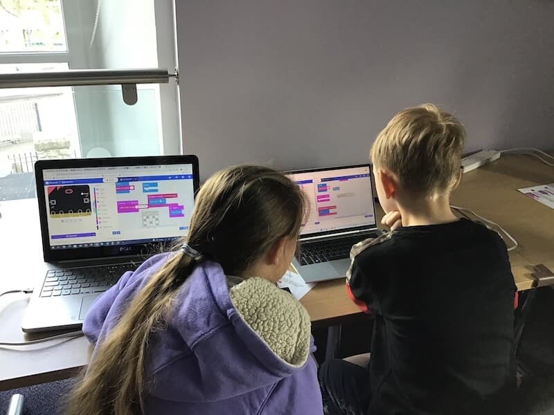 A girl and boy sitting together at laptops, both working on MakeCode
