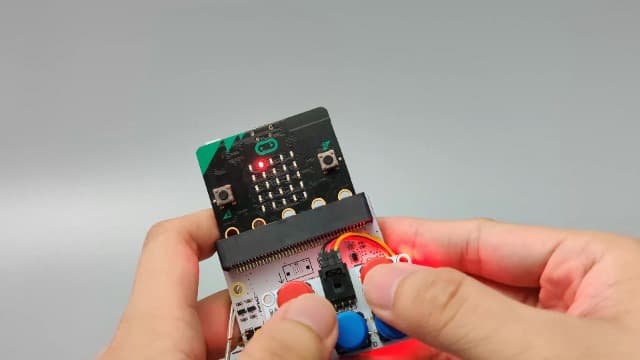 Hands interacting with a micro:bit Tinker Kit expansion project showing the Octopus:bit board and sensors