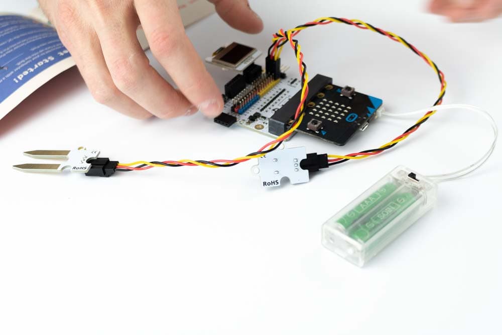 Hand interacting with a completed micro:bit Tinker Kit project showing sensors and outputs responding to touch