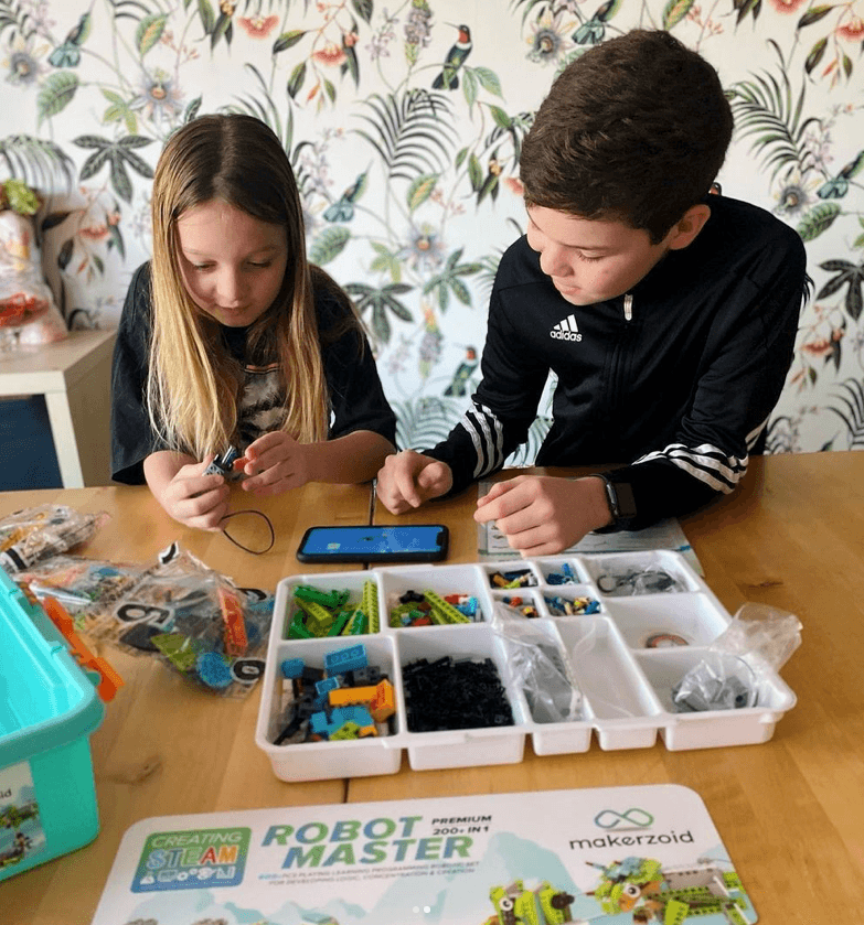 Two kids building together with Makerzoid and app on phone
