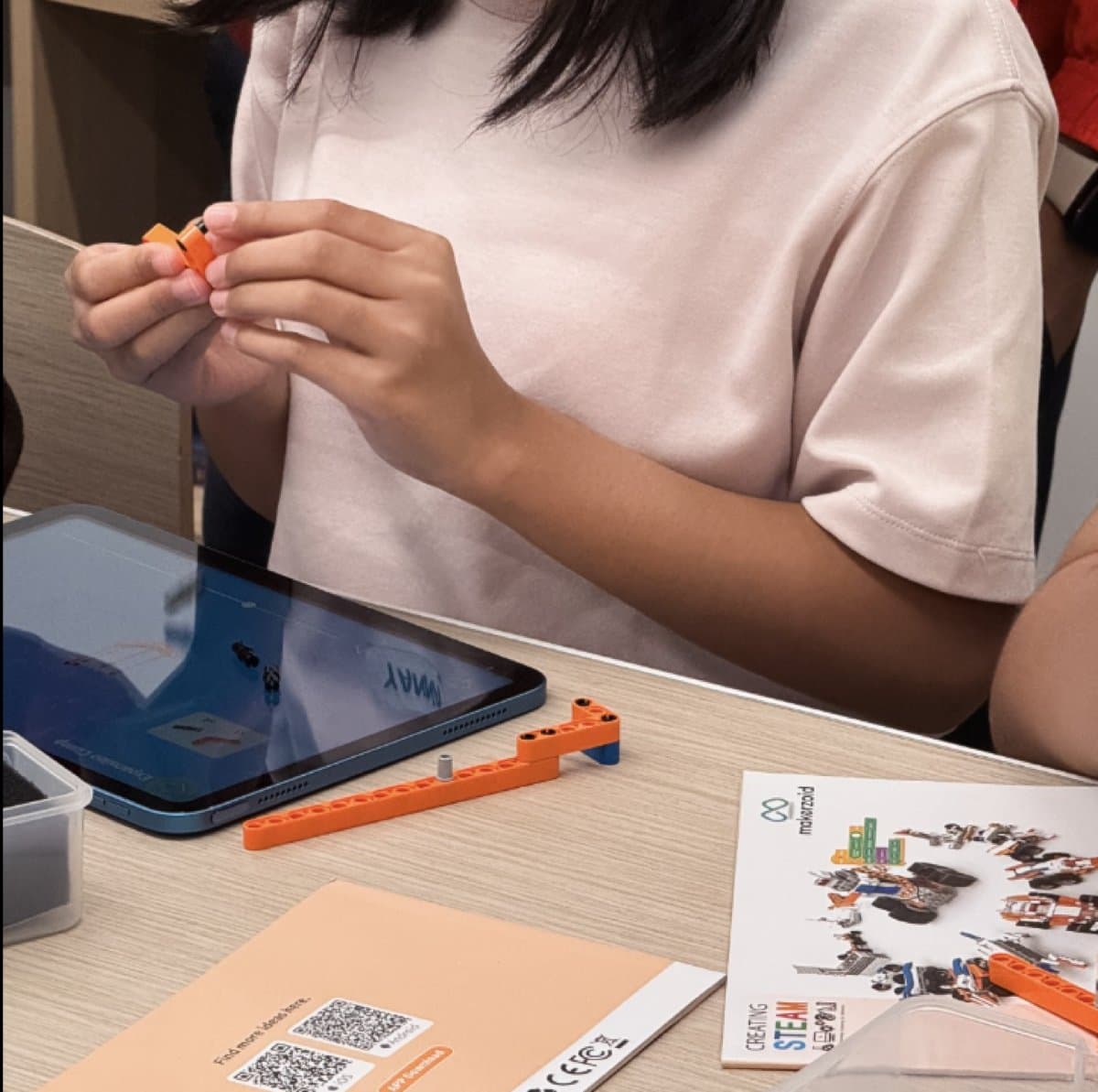 Child building with Makerzoid Superbot bricks with a tablet showing instructions nearby