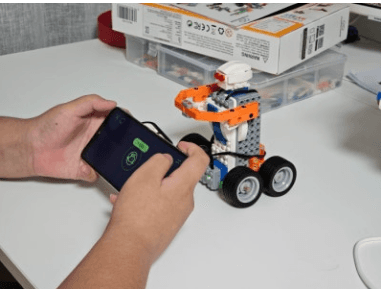 Hands holding a phone with the Makerzoid app open, a built robot in the foreground