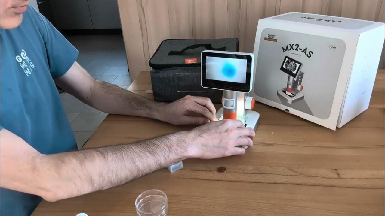 Adult hands holding the MX2-AS microscope after unboxing with all kit contents on table