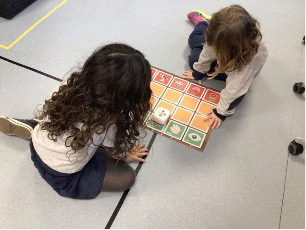 Two young girls sitting on floor coding with Tale-Bot Pro on interactive map