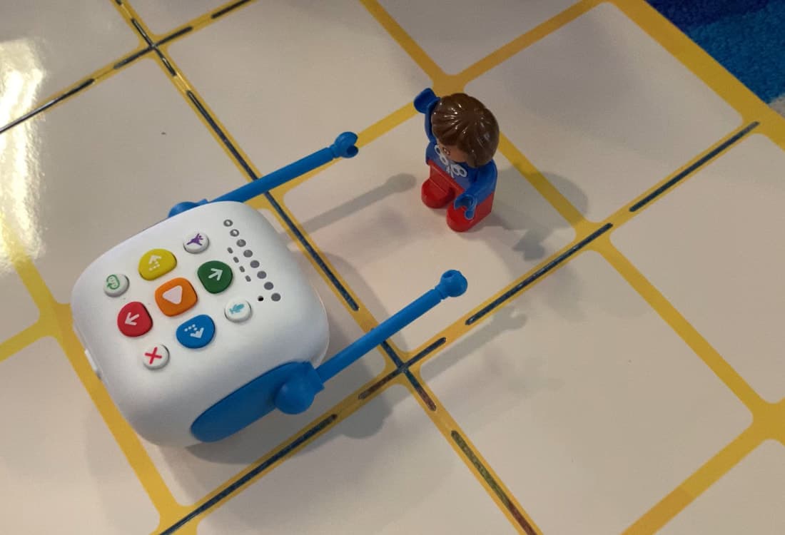 Tale-Bot Pro with arm attachments approaching a figure on an activity mat