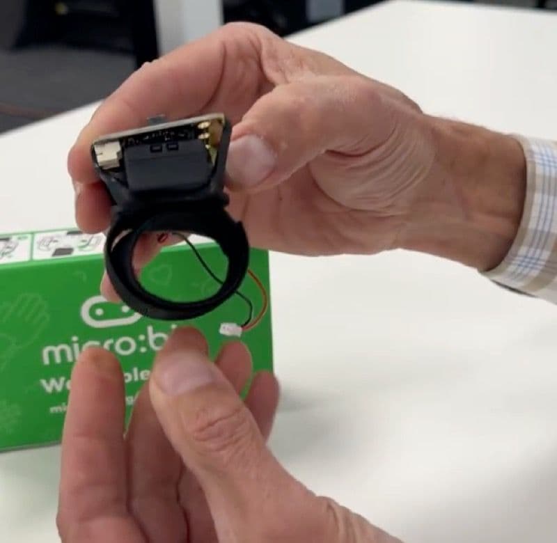 Hand holding a micro:bit with the wearable strap attached, box visible in background