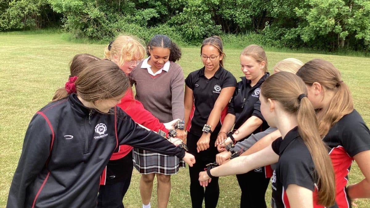 Group of children in a circle each wearing a micro:bit wearable strap on their wrists