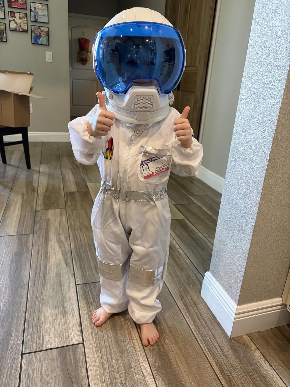 Child in white astronaut suit and NASA helmet giving two thumbs up