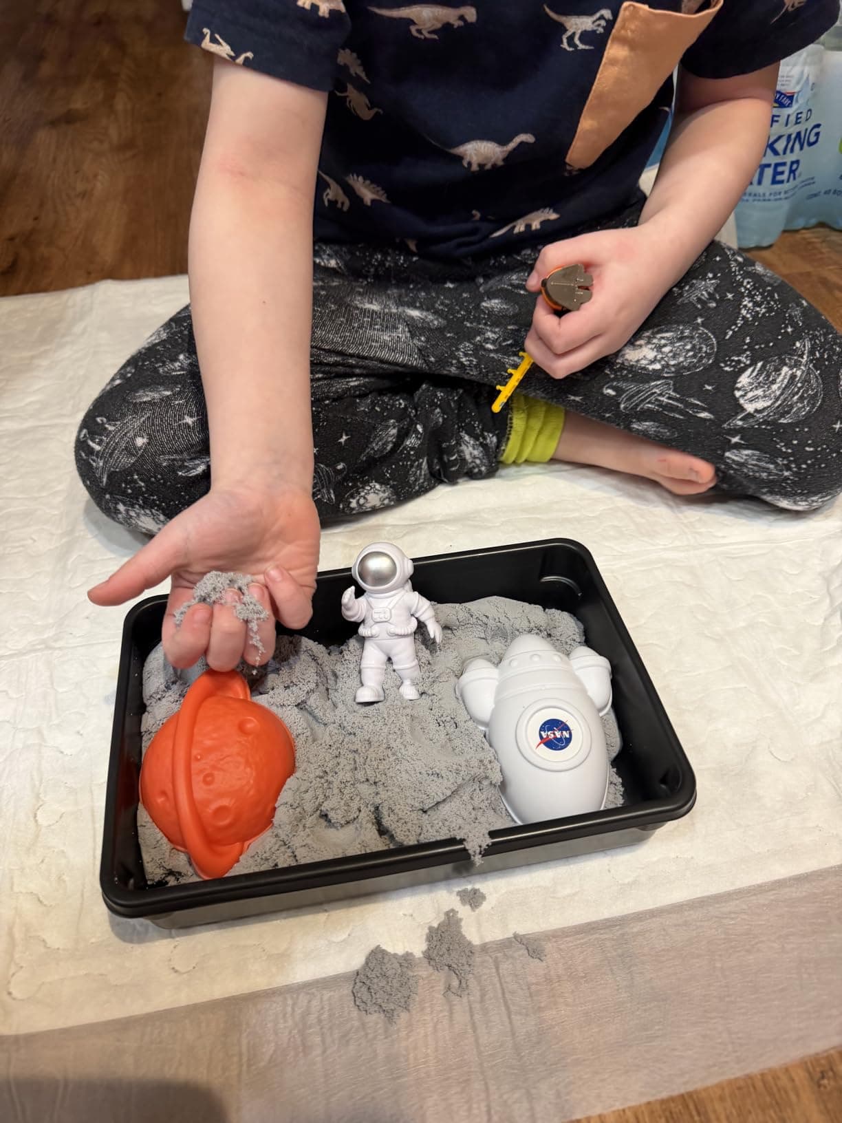 Boy sitting with the NASA Moon Sand kit in front of him, holding moon sand