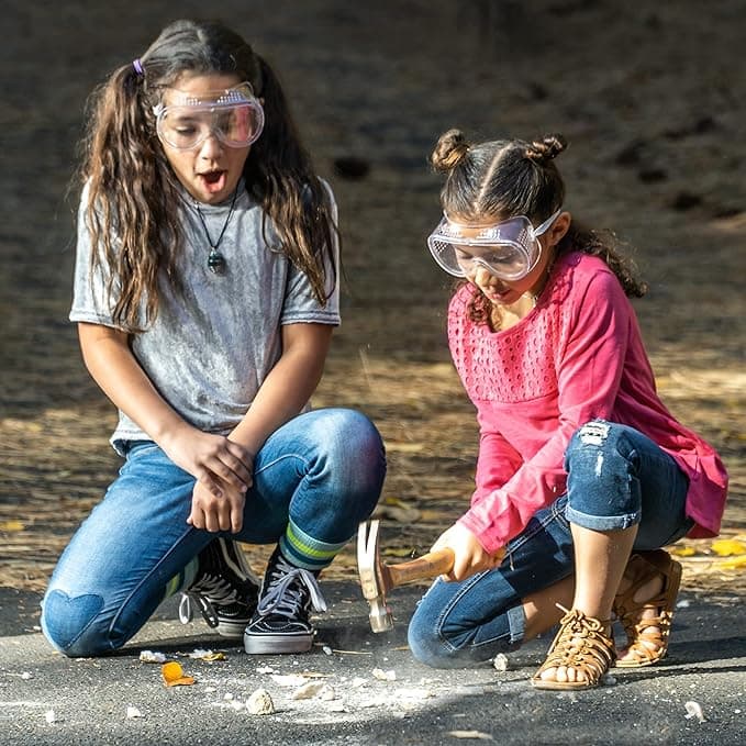 Child using a hammer to crack open a geode wearing safety goggles