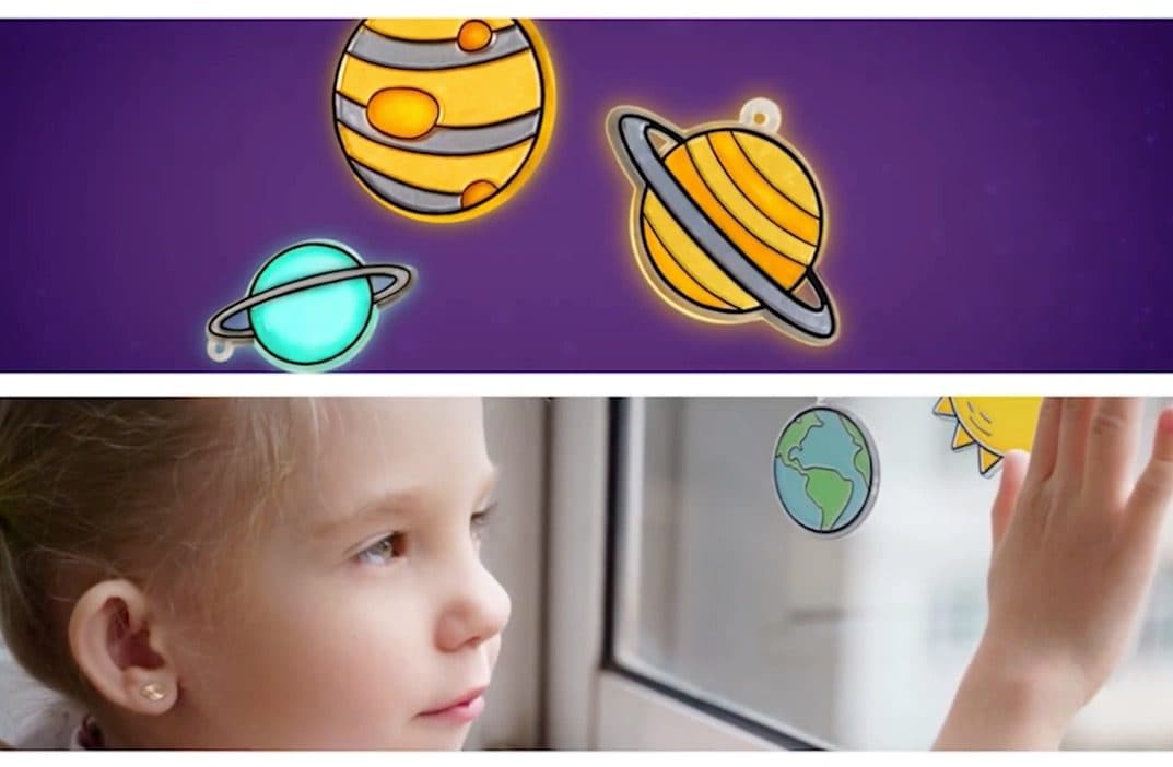 Child sticking a hand-painted glow-in-the-dark solar system onto a window