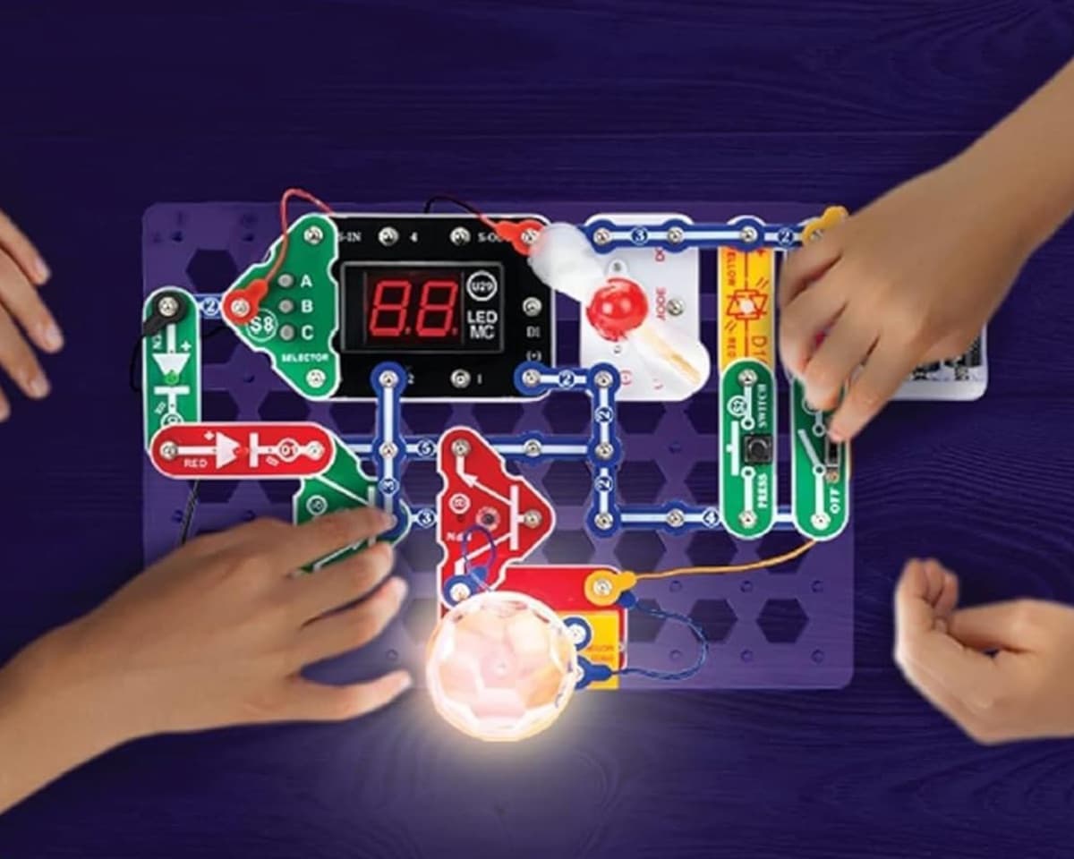 Top-down view of an illuminated Snap Circuits Arcade board with a child's hands at work