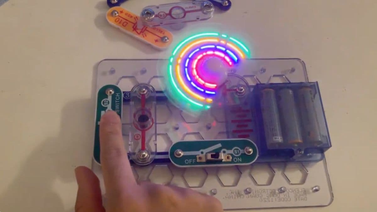 Finger pressing a switch on Snap Circuits board with the colourful light fan spinning