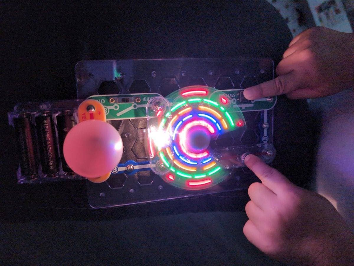Fingers pressing switches on Snap Circuits board with coloured lights glowing in the dark