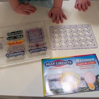 Snap Circuits Beginner kit unboxed with children's hands in the background