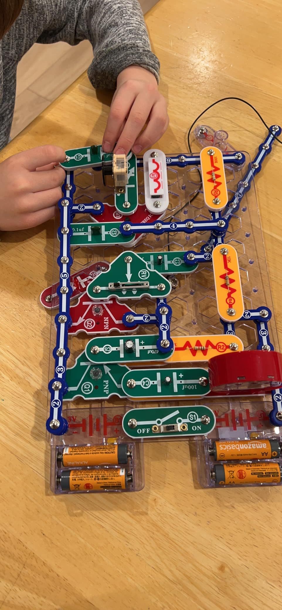 Child's hands actively building a Snap Circuits project on a wooden table