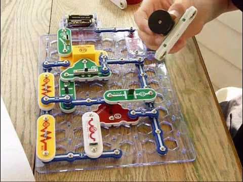 Hand placing a Snap Circuits module onto the grid board on a wooden table